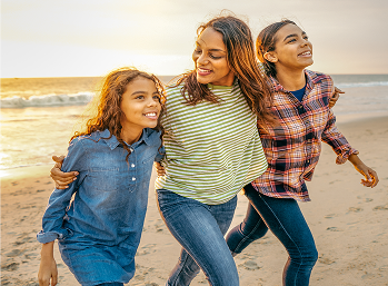 A mother with an arm around each of her two teen daughters, walking by the ocean.