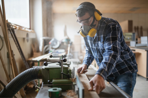 Worker with facemask on planning a piece of lumber 